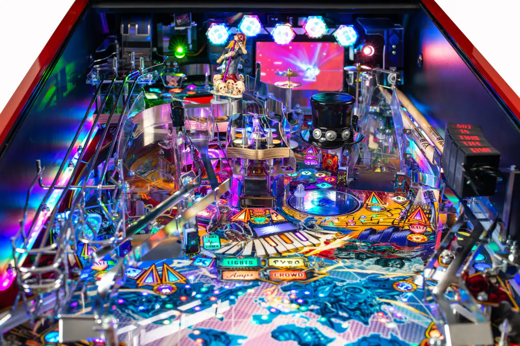 Le plateau du flipper Guns N’ Roses vu de biais, en entier : rampes chromées, lumières violettes et bleues, l’écran allumé au fond.