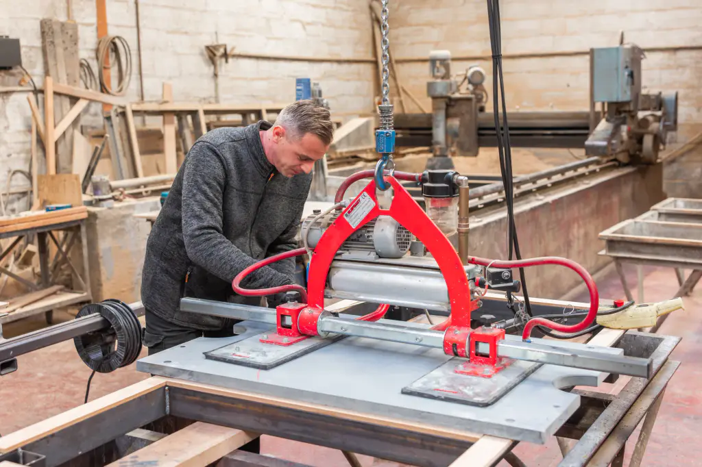 Dans l’atelier Maison Toulet, un artisan guide une ardoise de billard portée par un palonnier à ventouses.