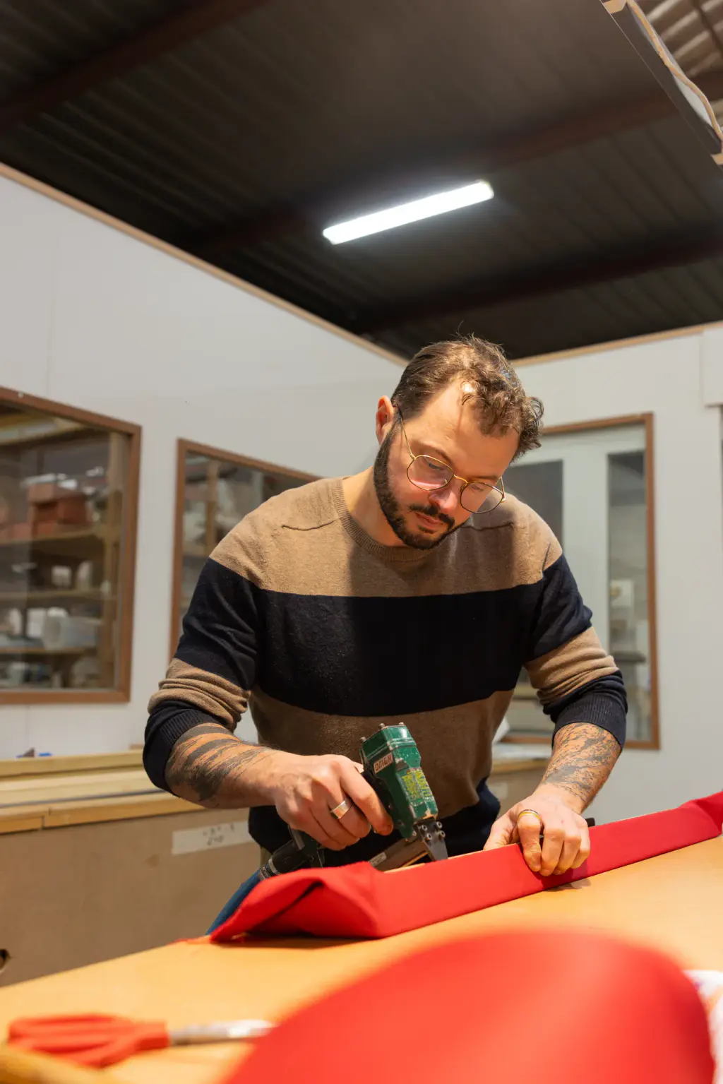 Dans l’atelier Maison Toulet, un artisan tend un drap rouge sur la bande d’un billard, visseuse en main.
