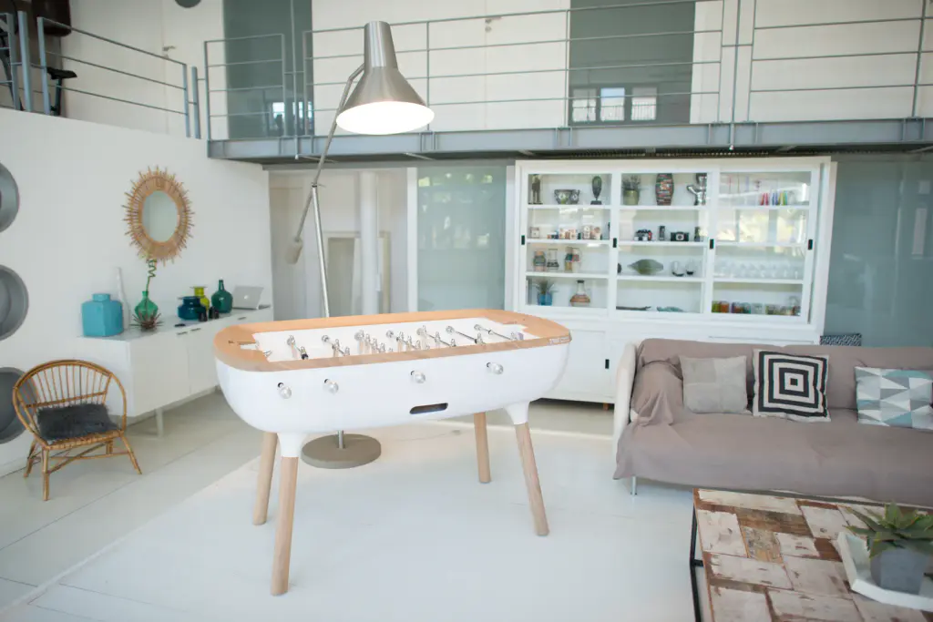 Baby-foot Maison Toulet à caisse blanche arrondie et pieds en bois clair, au milieu d’un séjour lumineux à mezzanine.