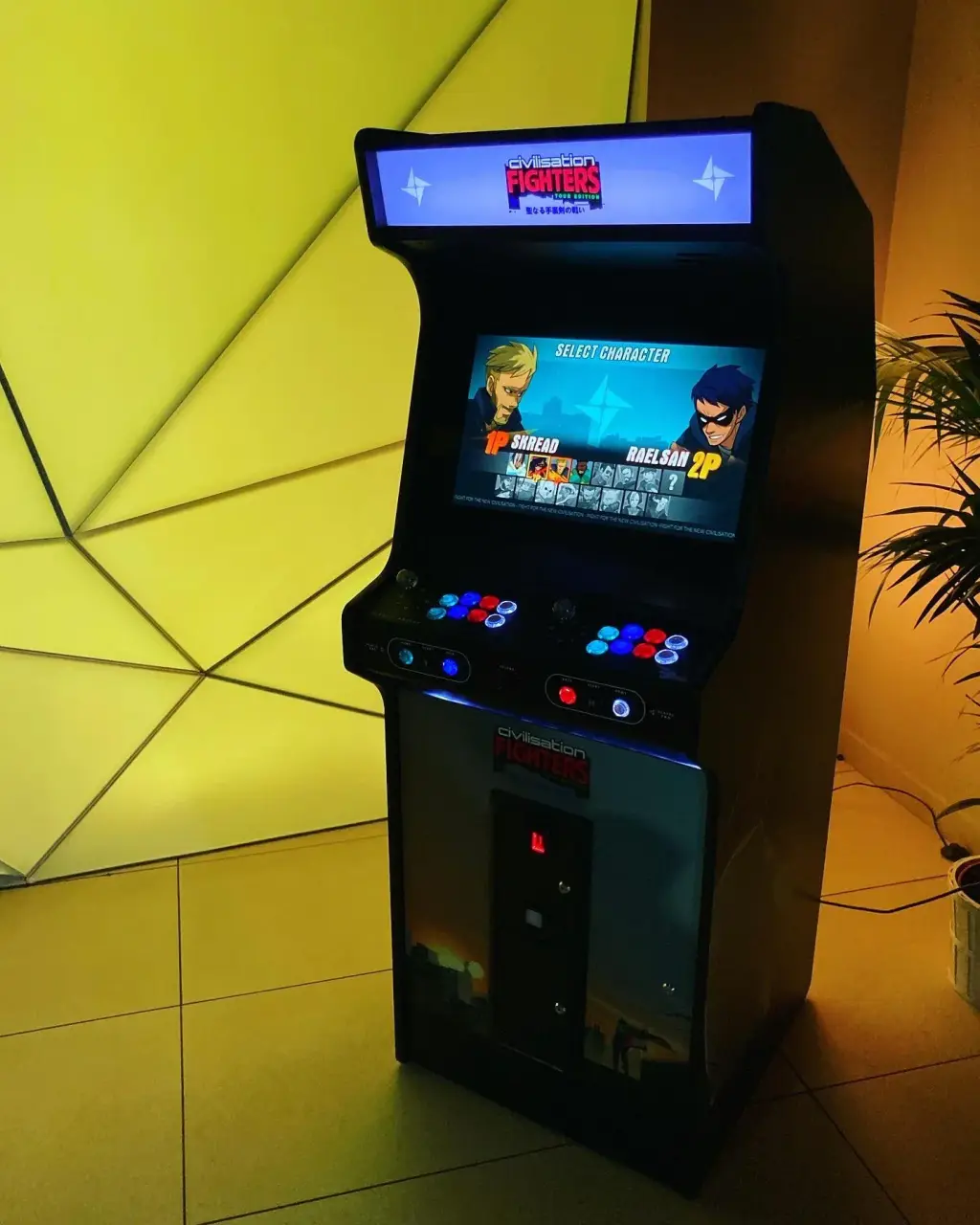 Une borne d’arcade Neo Legend debout, noire, vue de trois quarts : fronton éclairé, écran de sélection des personnages, pupitre à deux manches et boutons lumineux ; mur jaune lumineux et palmier derrière.