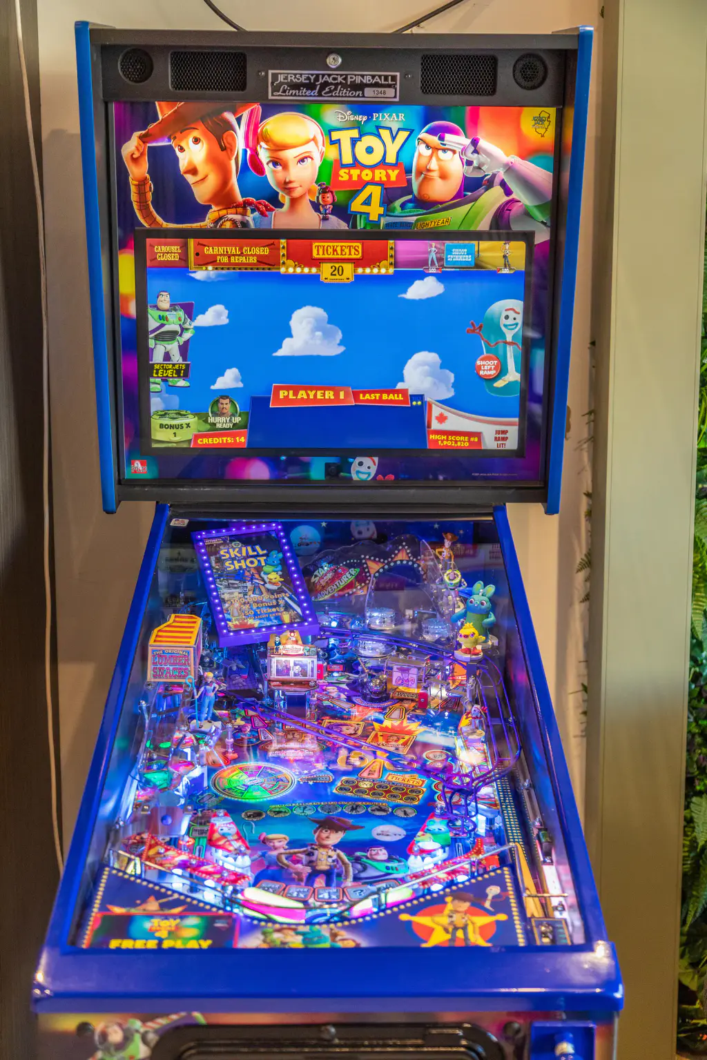 Le flipper Toy Story 4 de Jersey Jack Pinball vu de face au showroom de Porticcio : fronton à écran sur un ciel bleu à nuages, plateau allumé sous la vitre, caisse et montants bleus.