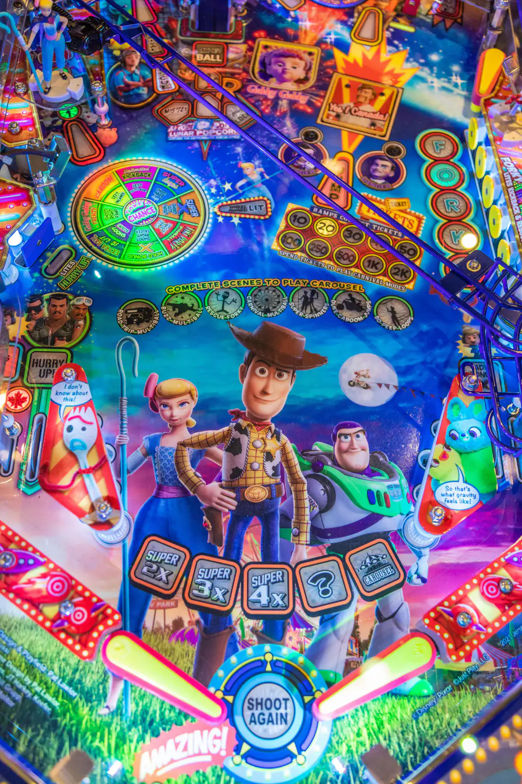 Plateau du flipper Toy Story 4 vu du dessus : les deux batteurs jaunes et roses, l’insert « Shoot again », une roue multicolore, une rampe en fil d’acier violet et les personnages du film peints au centre.