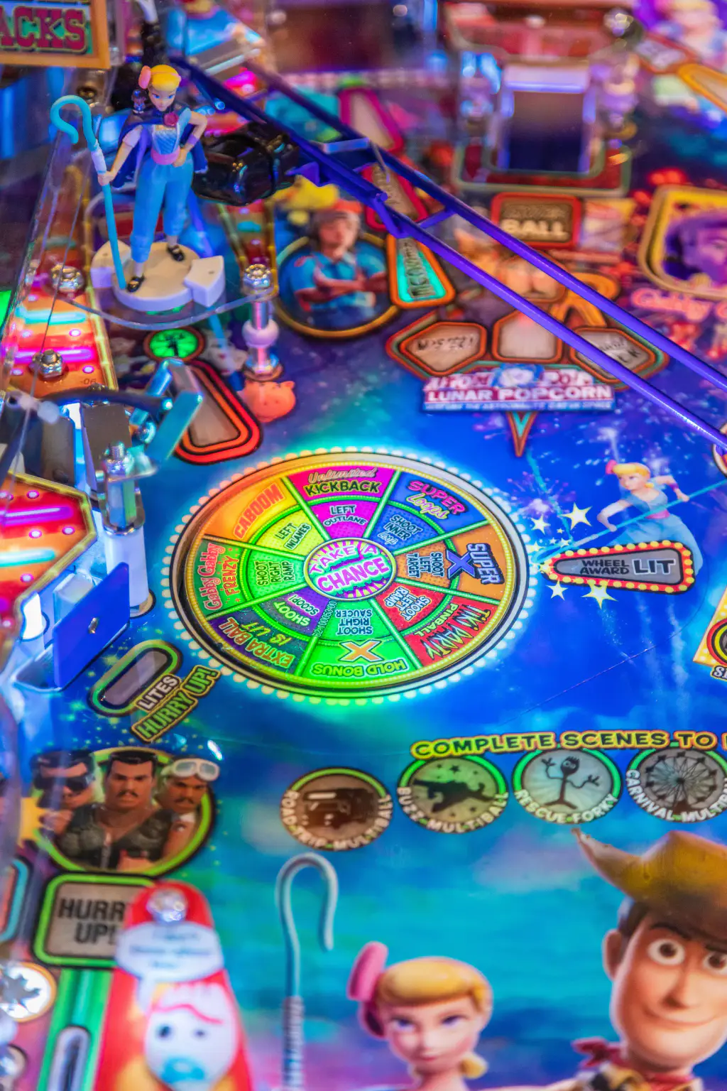 Gros plan sur le plateau du flipper Toy Story 4 : une roue de loterie multicolore éclairée, une figurine de bergère en bleu sur son socle, une rampe violette et des inserts lumineux.