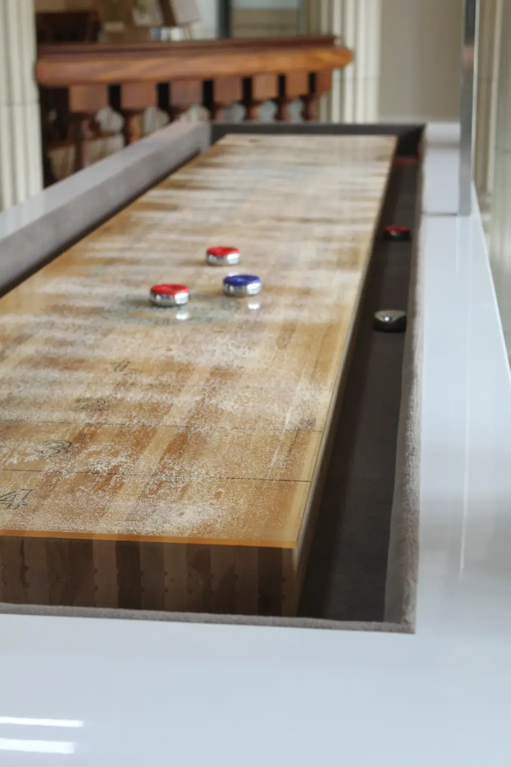 Shuffleboard Maison Toulet vu dans sa longueur : plateau de bois verni, palets rouges et bleus posés au bout.