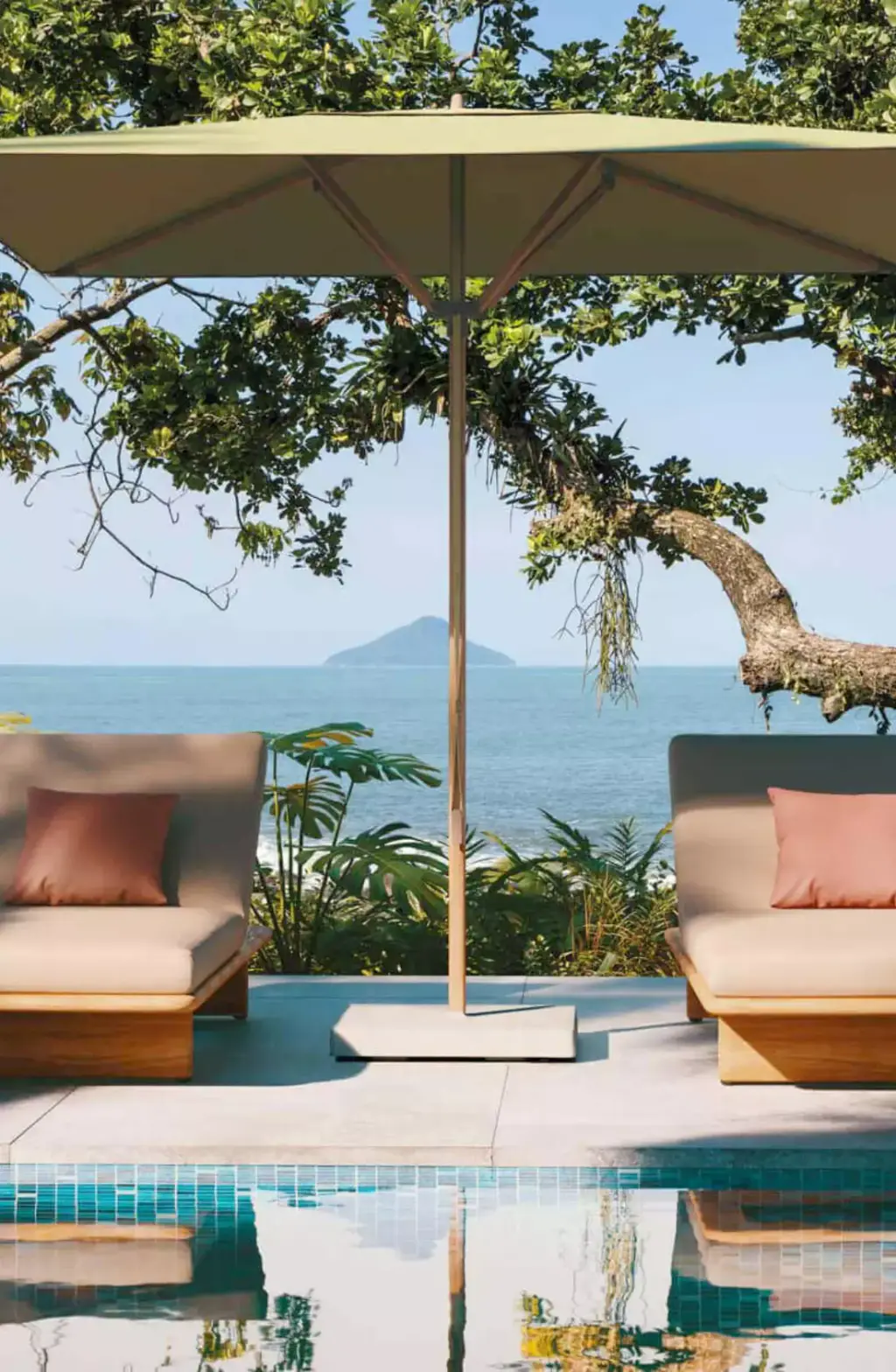 Visuel de fournisseur : parasol et fauteuils bas au bord d’un bassin, la mer et une île au fond.