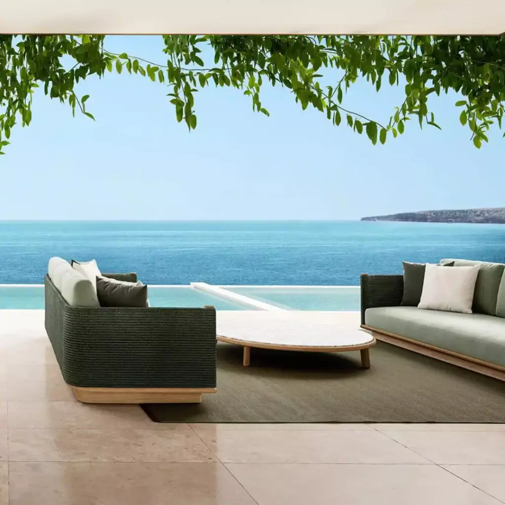 Visuel de fournisseur : canapés d’extérieur en corde tressée verte et table basse ronde sur une terrasse en pierre claire, sous une treille feuillue, mer turquoise à l’horizon.