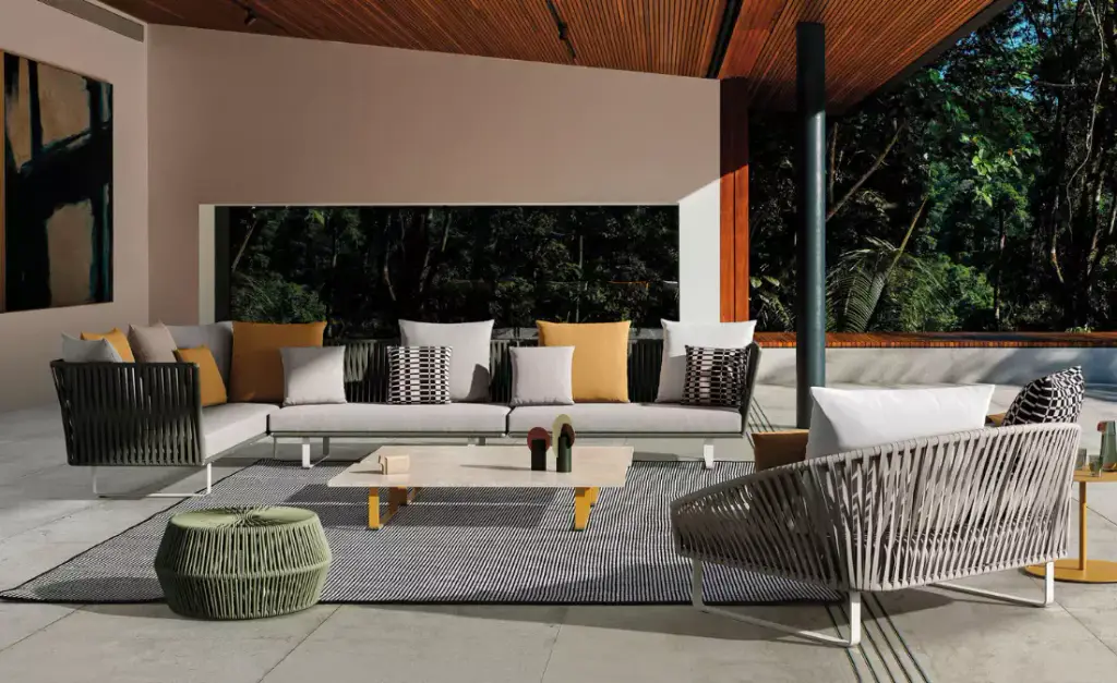 Visuel de fournisseur : salon d’extérieur sous un auvent à plafond de bois : canapé d’angle et fauteuils à structure cordée, coussins jaunes et rayés, pouf vert tressé, tapis graphique.