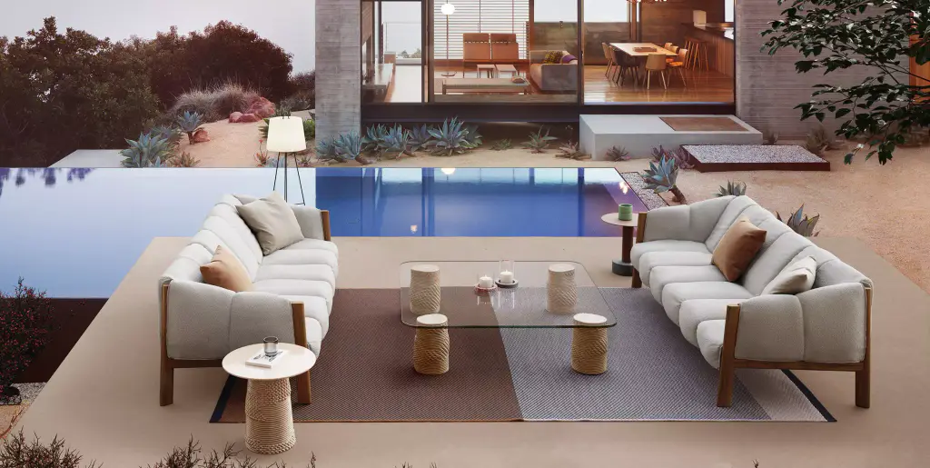 Visuel de fournisseur : deux canapés d’extérieur à structure bois et coussins clairs, face à face autour d’une table basse en verre posée sur un tapis, au bord d’une piscine devant une maison vitrée.