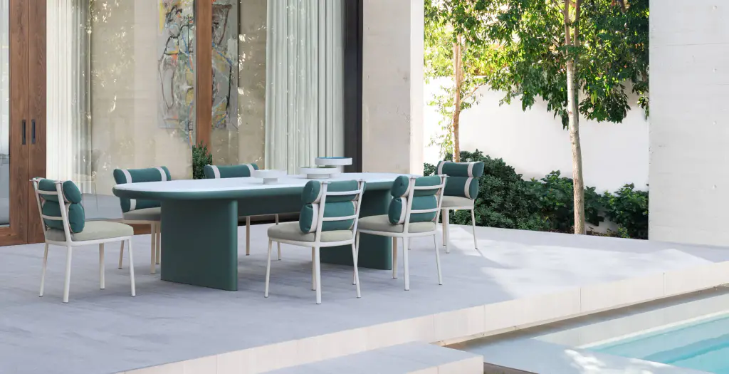 Supplier image: teal dining table and chairs with matching cushions in a white patio planted with trees, beside a pool.