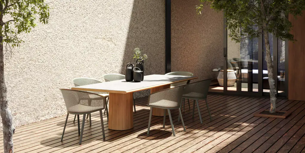 Visuel de fournisseur : table à manger au piètement en bois et fauteuils cordés sur une terrasse en lames de bois, devant un mur crépi clair traversé par l’ombre d’un arbre.
