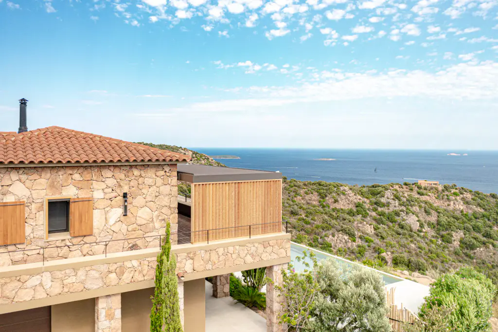 Drone view: stone house, wooden privacy screen on the terrace, sea on the horizon.