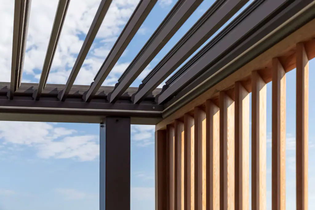Lames de pergola anthracite ouvertes et lames de bois verticales, sous un ciel moutonné.