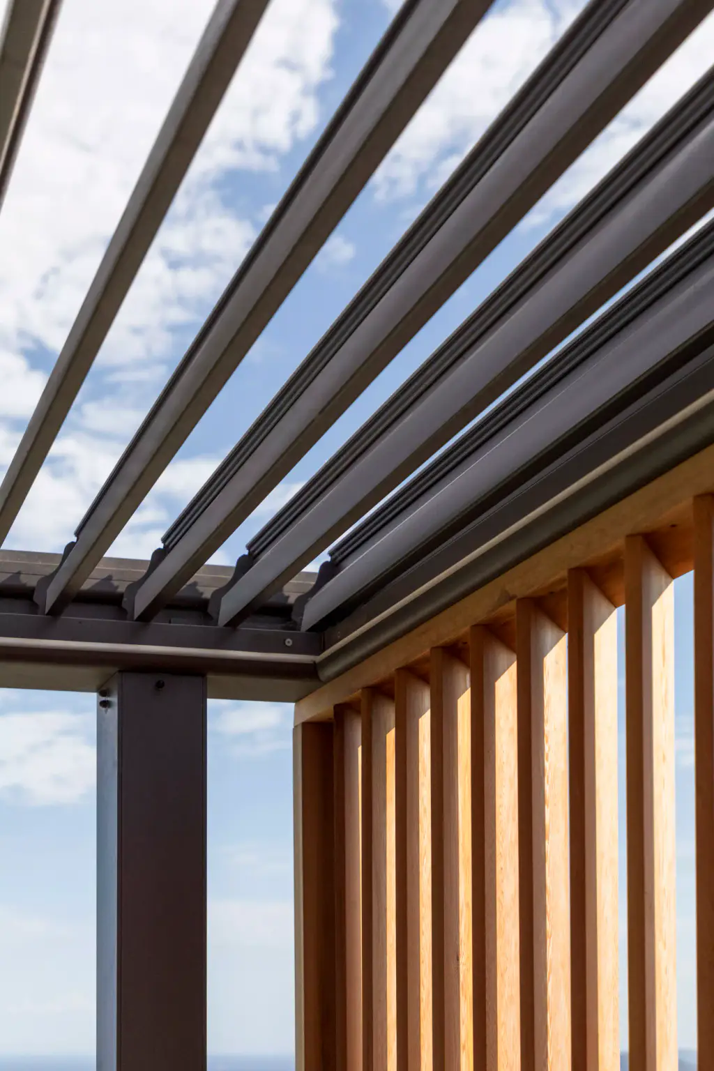 Vertical corner detail: anthracite pergola louvres open and vertical wooden slats.