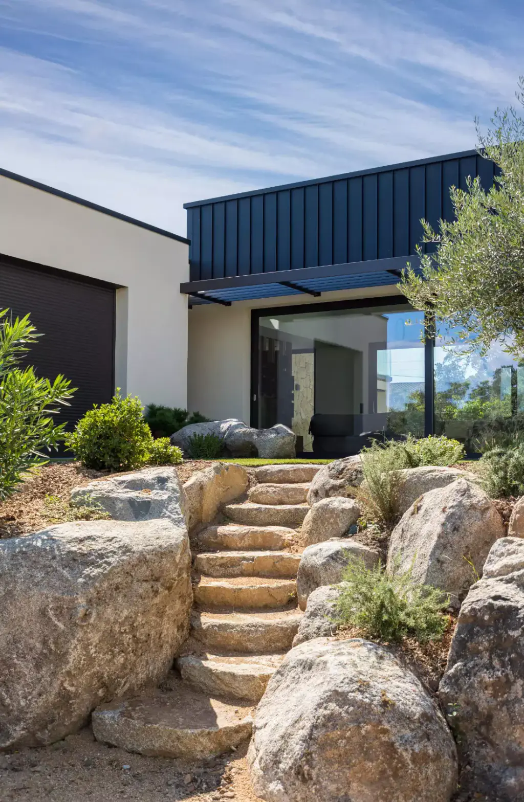 Stone staircase between rocks, villa with black zinc cladding above.