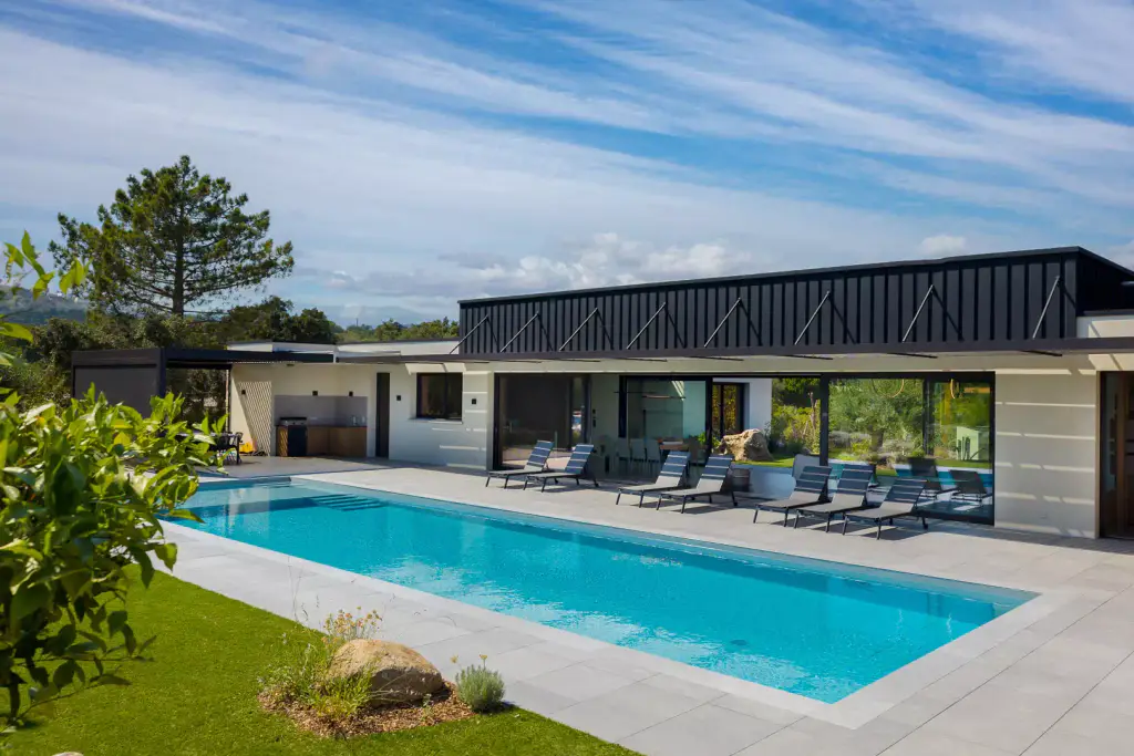 Casa Ghjovi: the single-storey villa with black cladding, its long pool and its loungers.