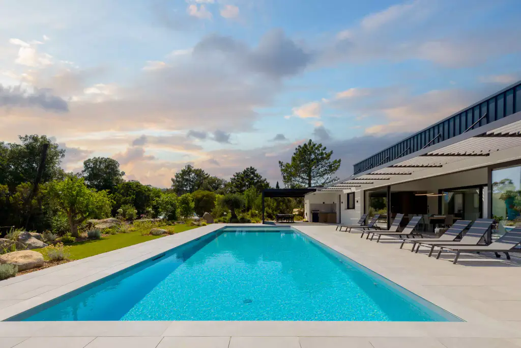 Pool in perspective under a late-afternoon sky, villa and brise-soleil on the right.