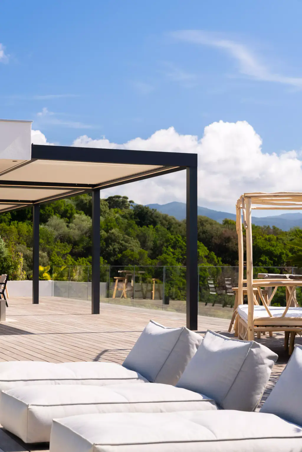 Blurred white sunloungers in the foreground, pergola and wooden four-poster daybed behind, wide sky.