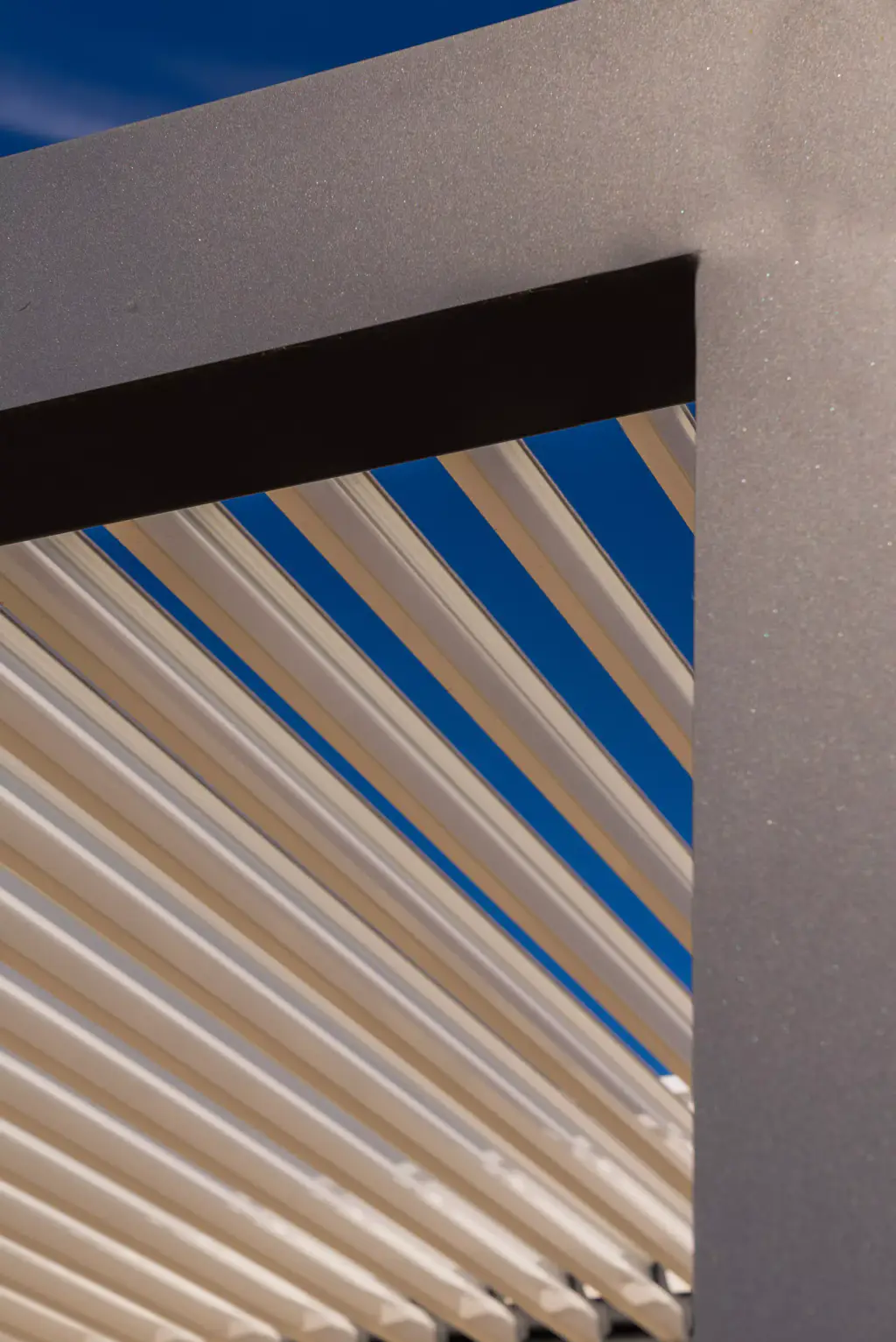 Corner detail: anthracite frame, light-coloured louvres on the diagonal, a patch of blue sky.