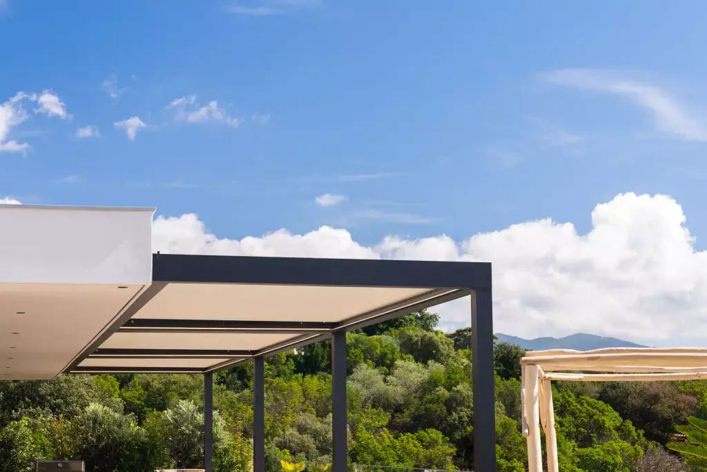 The pergola from afar, louvres closed, under a wide sky of cumulus; a strip of maquis.