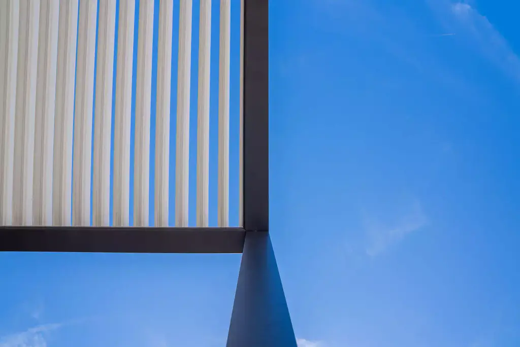 Graphic detail: vertical white louvres, anthracite post and a flat expanse of blue sky.