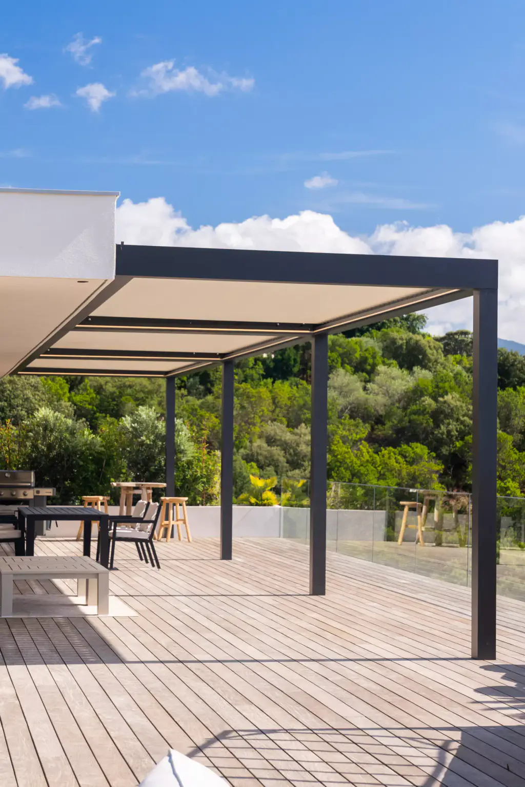 Cantilevered pergola seen from the deck, wide sky, glass balustrade, table beyond, blurred edge in the foreground.