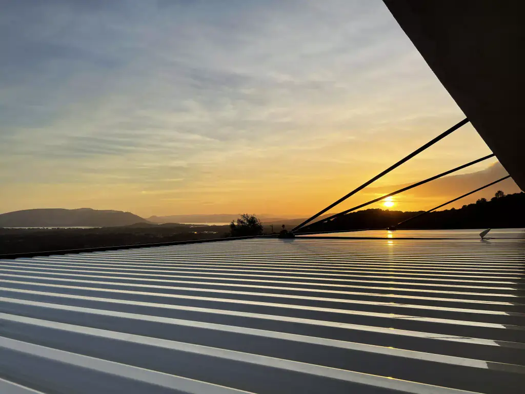 Casa Marcuri: sunset over the top of a pergola with light louvres, the structure in silhouette, the gulf beyond.