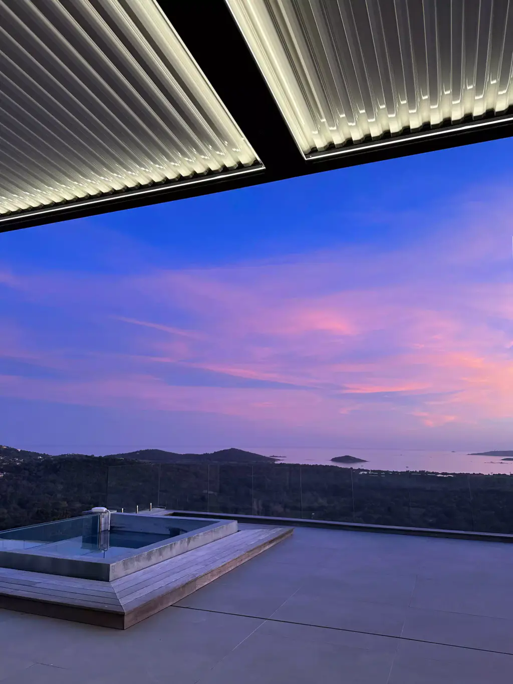 Pergola à lames avec ruban LED périphérique allumé, ciel rose et violet au crépuscule, jacuzzi encastré, golfe.