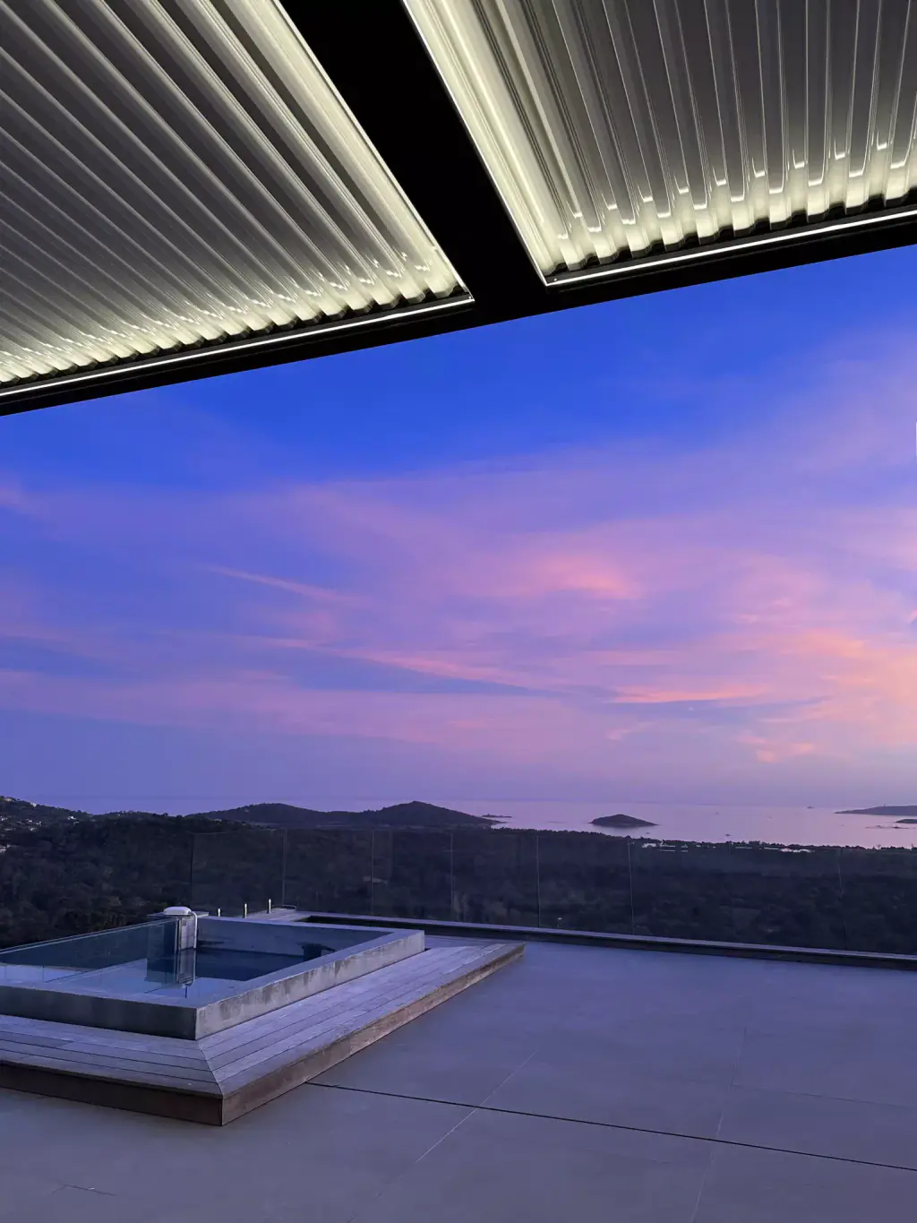 Pergola à lames avec ruban LED périphérique allumé, ciel rose et violet au crépuscule, jacuzzi encastré, golfe.