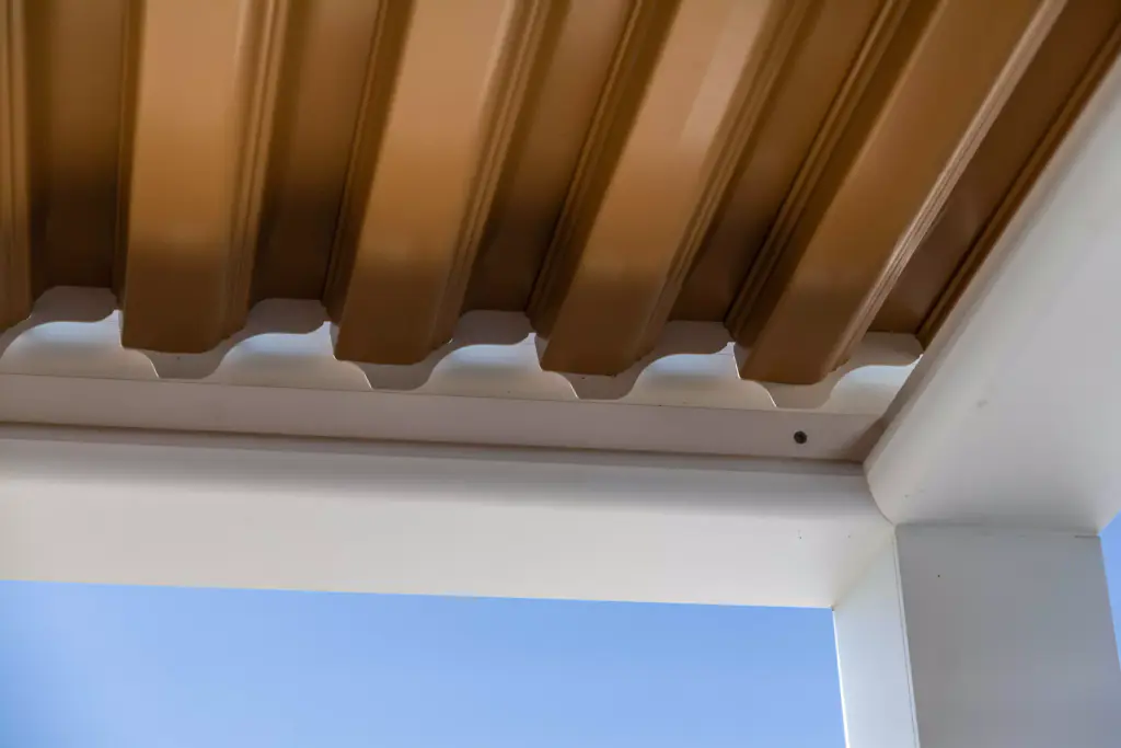 Détail d’angle intérieur : les lames effet bois, le chéneau et le poteau blancs, le ciel bleu.