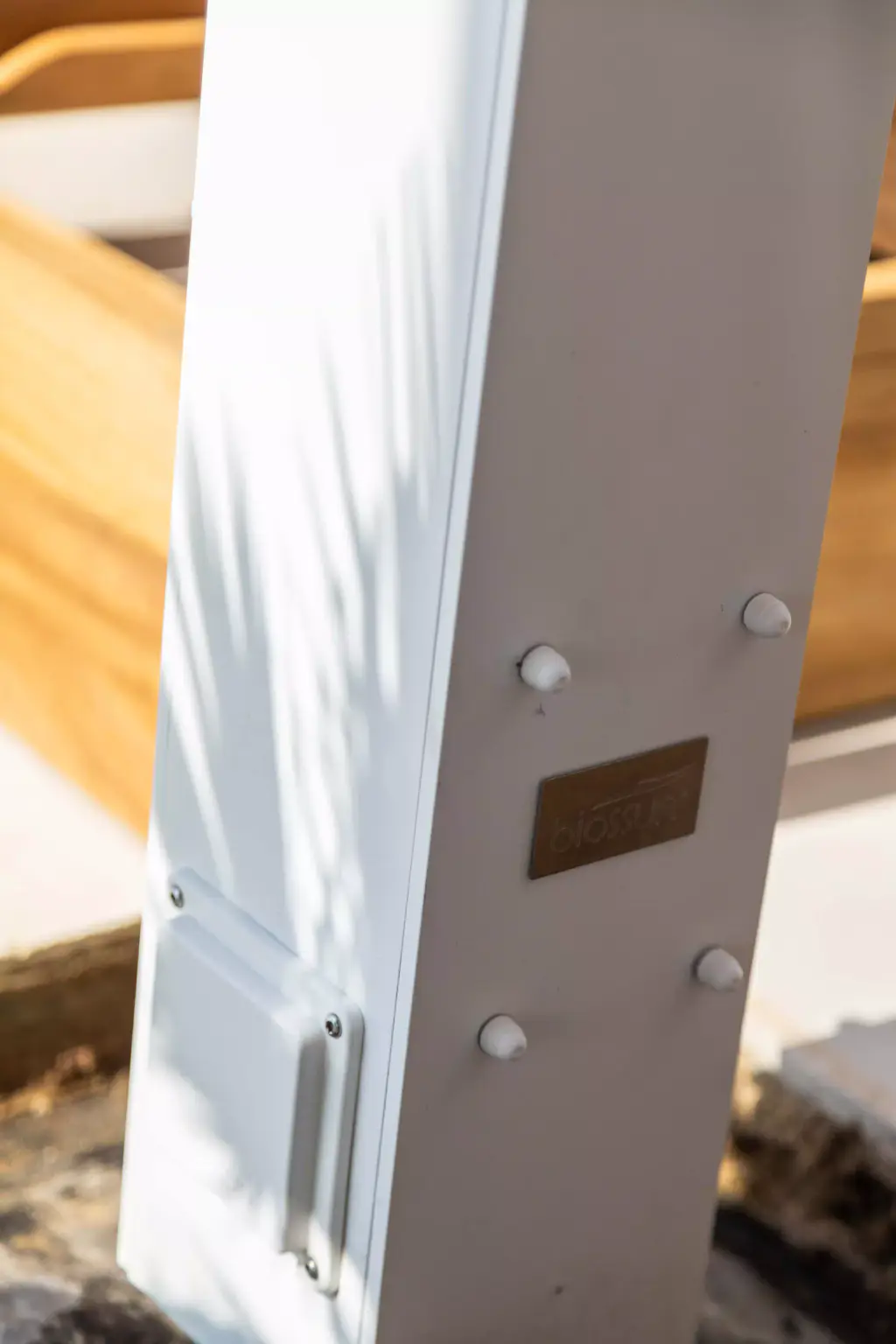 Détail du poteau blanc : plaque du fabricant et visserie, ombre d’une palme.