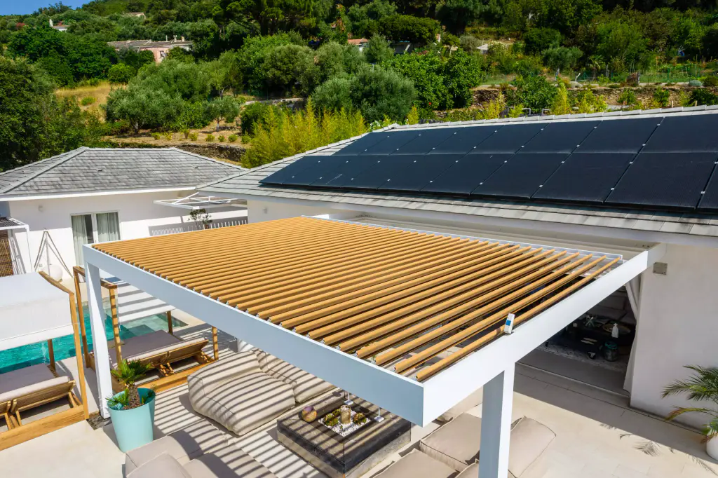 Vue drone de trois quarts, lames fermées : pergola, salon, panneaux solaires, maquis.