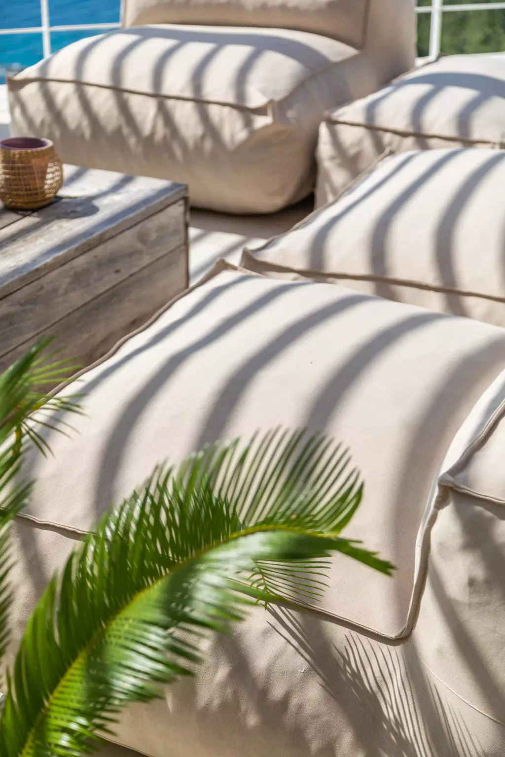 Gros plan d’un pouf rayé d’ombres, palme en amorce.