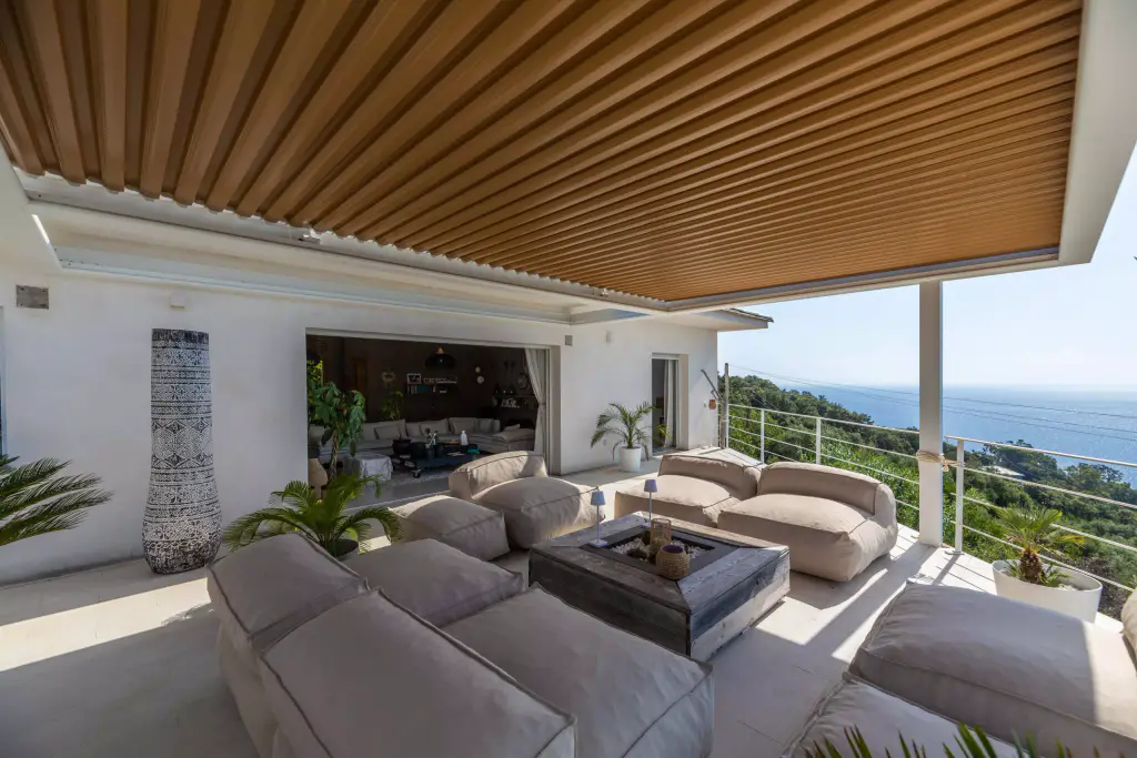 Sous la pergola vers la villa, lames fermées, grand vase à gauche.