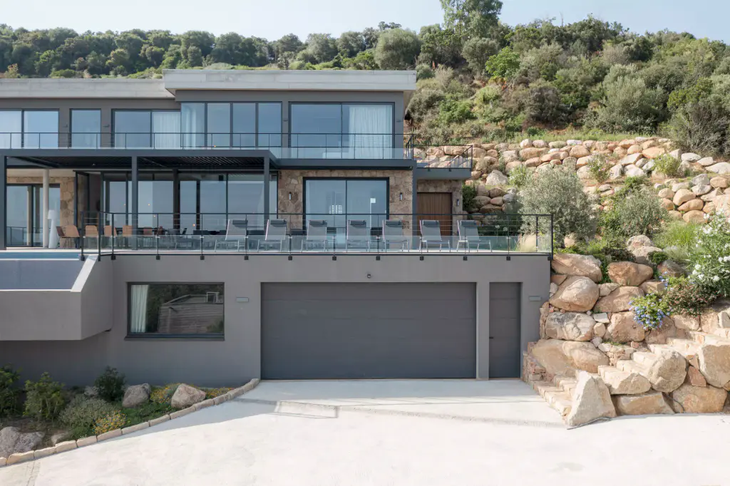 Front drone view of the two-level villa, garage and rock embankment.