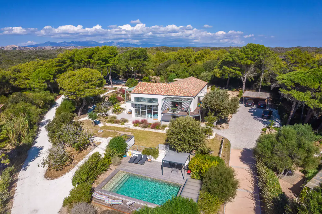 Casa Pinu vue du ciel : la maison blanche et ses pergolas vertes sous les pins, la piscine au premier plan.