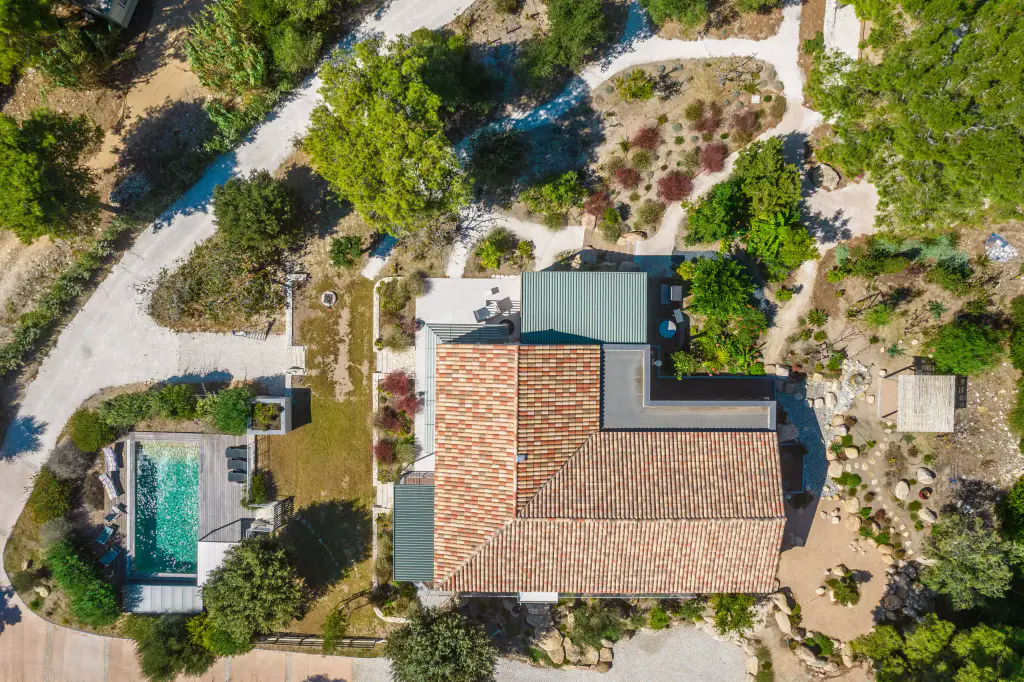 Vue drone à la verticale : toit de tuiles en L, toiture verte de la pergola fermée en haut, piscine turquoise et deck en bois à gauche, jardin de rocaille tout autour.