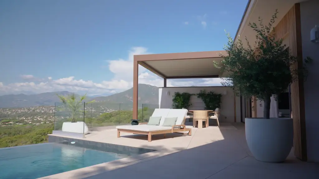 Le film de la Casa Petra : la villa vue par drone, sa façade, la pergola brun cuivré et la piscine ; les lames qui s’ouvrent, leurs ombres au sol et le soleil qui passe entre elles ; les terrasses, un voilage devant le panorama, la table de repas, un citronnier ; les lames contre le ciel bleu ; la piscine à débordement devant les montagnes.