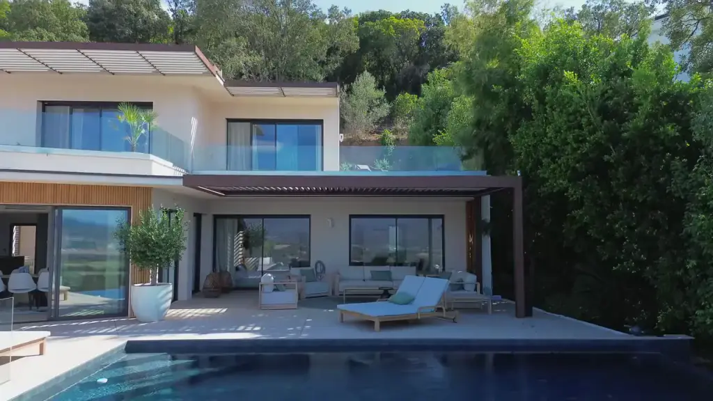 Film : la façade d’une villa et sa pergola bioclimatique, les lames qui s’ouvrent au-dessus du salon, puis la piscine à débordement.