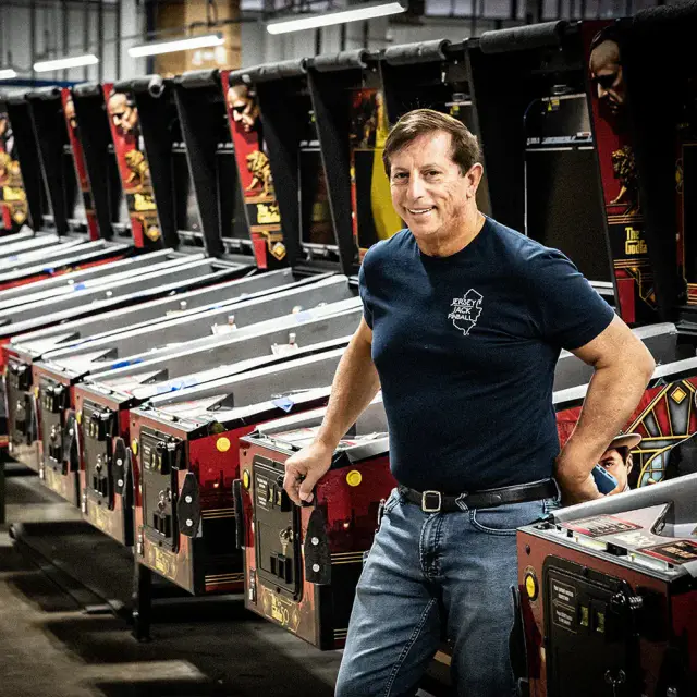 Jack Guarnieri, fondateur de Jersey Jack Pinball, au milieu de rangées de caisses de flipper dans son usine.