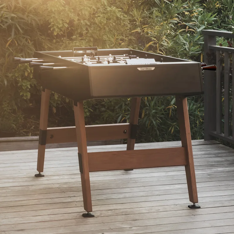 Baby-foot Origin Outdoor de Cornilleau, noir, sur ses pieds en bois de Moabi, sur une terrasse en bois.