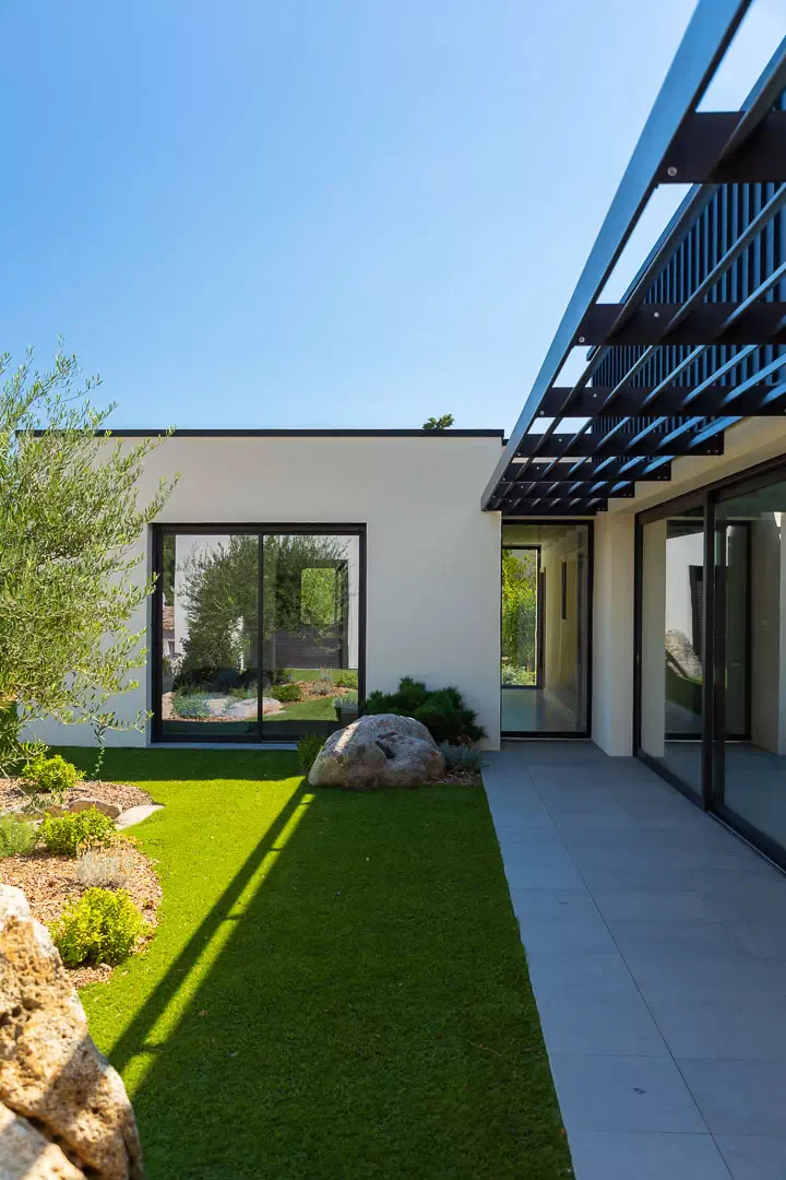 White facade, brise-soleil canopy, lawn and olive tree.