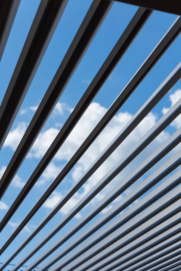 Anthracite brise-soleil louvres seen from below against a cloudy sky.